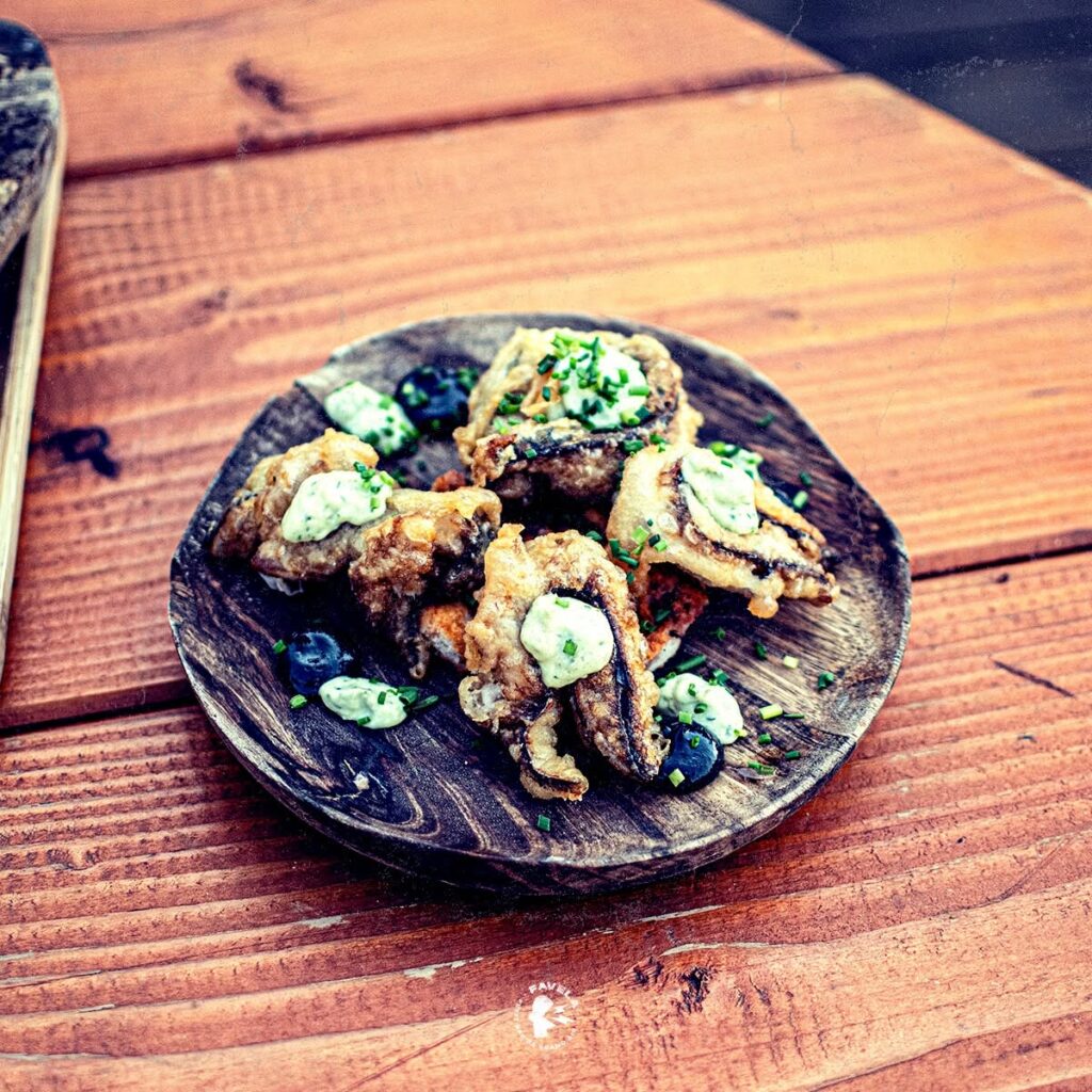 Beignets Croustillants avec Crème aux Herbes Fraîches Beignets croustillants garnis de crème aux herbes et ciboulette sur une assiette en bois rustique.