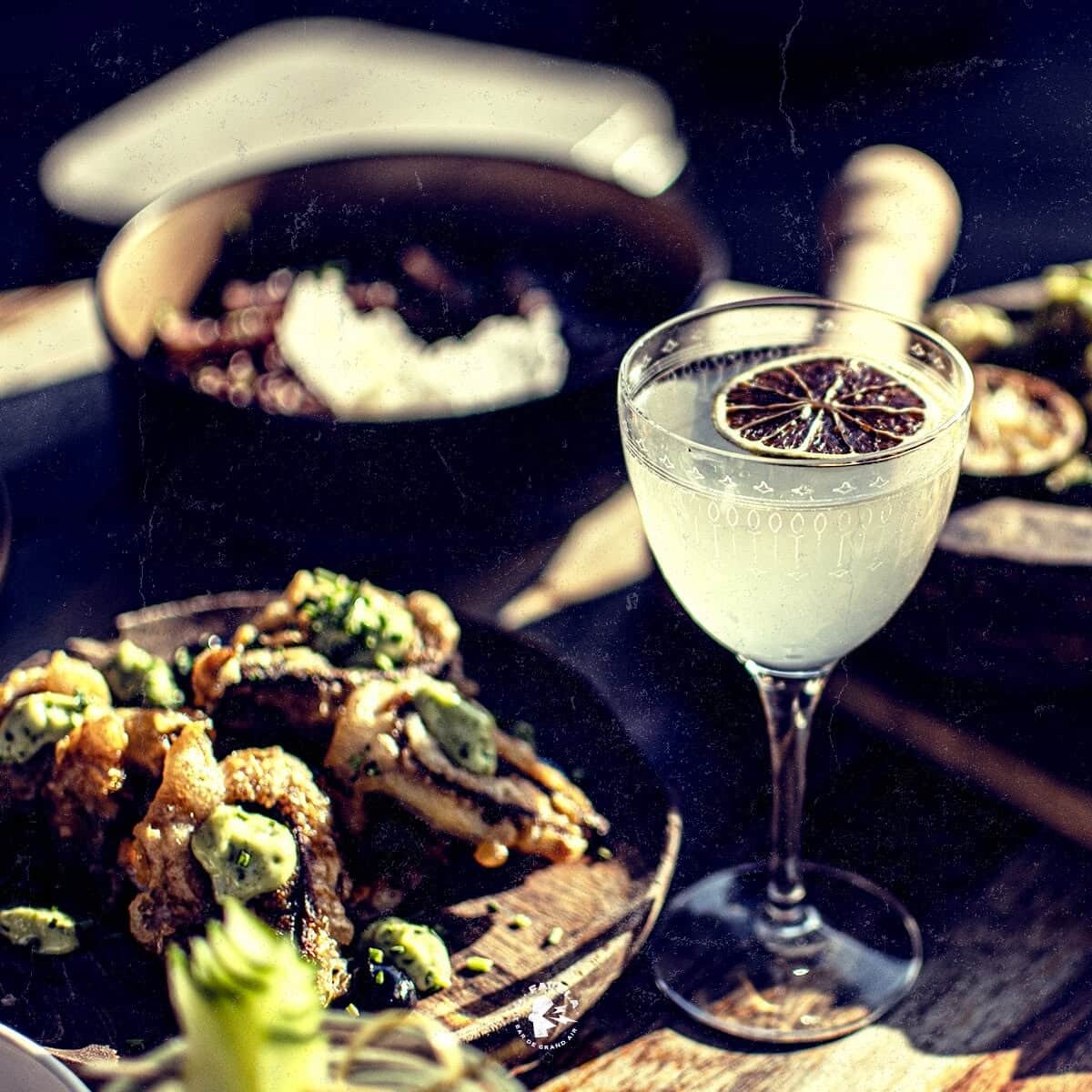 Cocktail au citron séché et bouchées frites avec sauce verte sur table sombre.