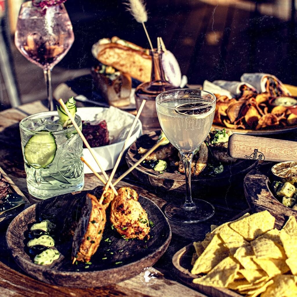 Cocktails et Tapas Gourmands en Terrasse au Favela Brochettes de poulet, nachos et cocktails colorés sur une table en bois en terrasse au Favela.