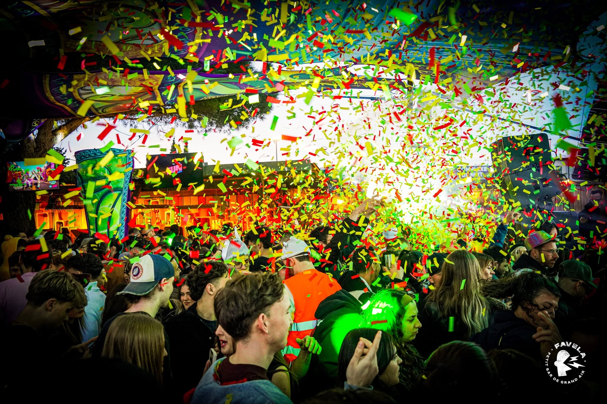 Foule célébrant sous des confettis au Favela Petit Bar de Grand Air. Lumières vertes et ambiance festive.