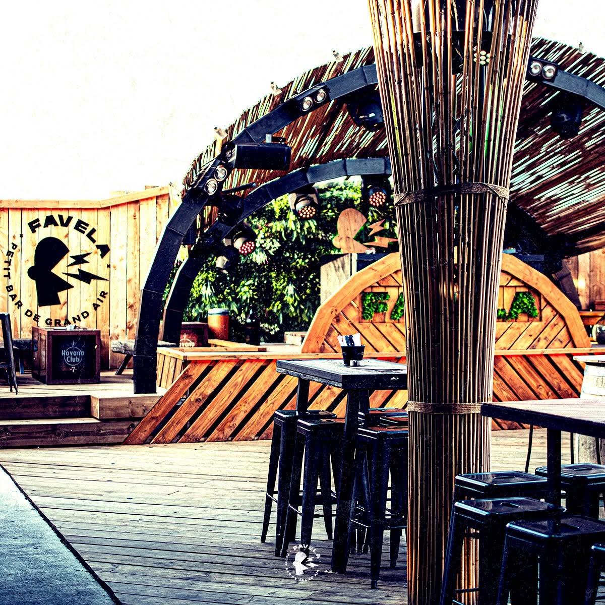 Terrasse bois du Favela Petit Bar de Grand Air avec tabourets noirs et décor bambou sous dôme lumineux.