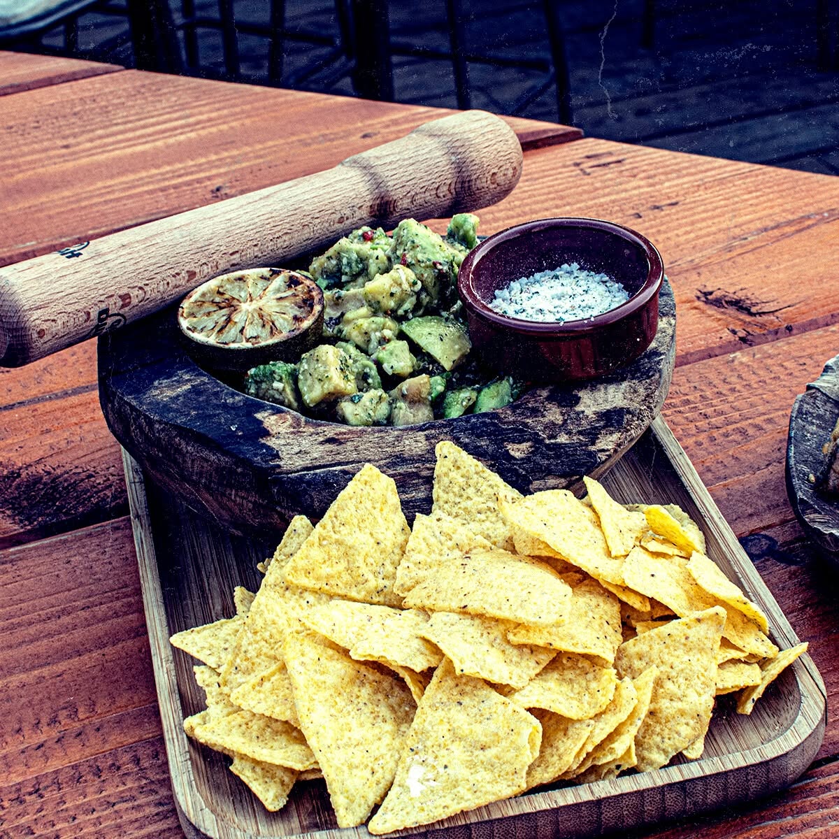 Guacamole, chips de maïs et citron grillé servis dans un mortier en bois rustique.