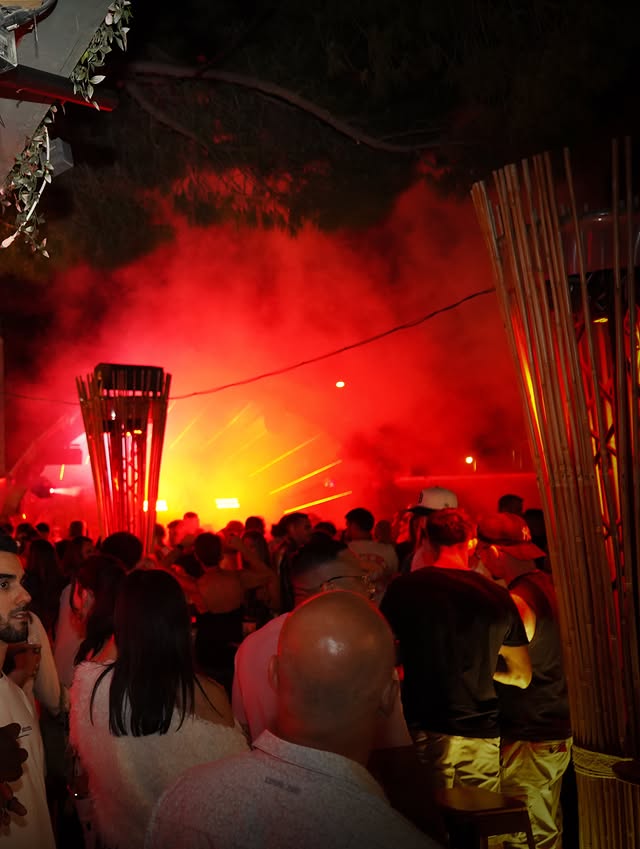 Foule dansant dans un club sous une épaisse fumée rouge et des jeux de lumière vibrants.